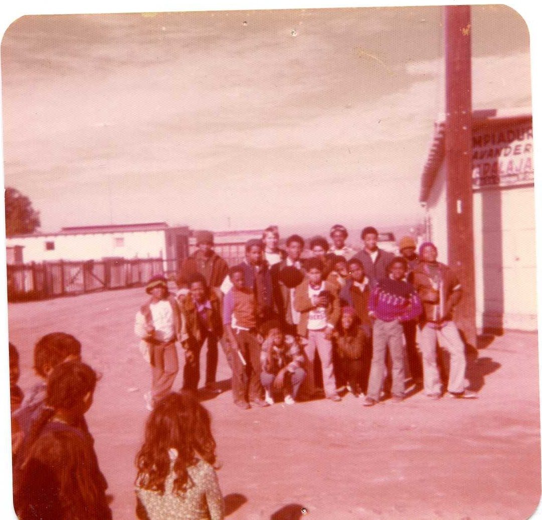 Boys and young men standing together in a dirt yard beside a building in Tijuana
